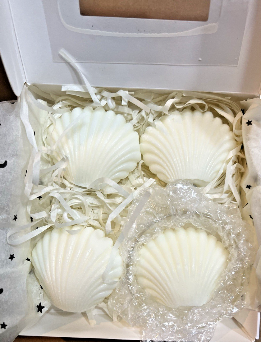 Four handmade seashell-shaped floral scented candles displayed with one small clear glass holder on a decorative surface