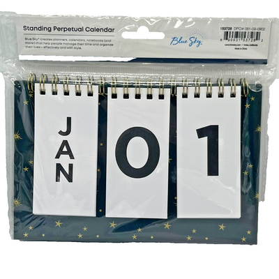 Blue Sky standing perpetual desk calendar with black base, gold starburst accents, and gold twin-wire binding showing flip date cards