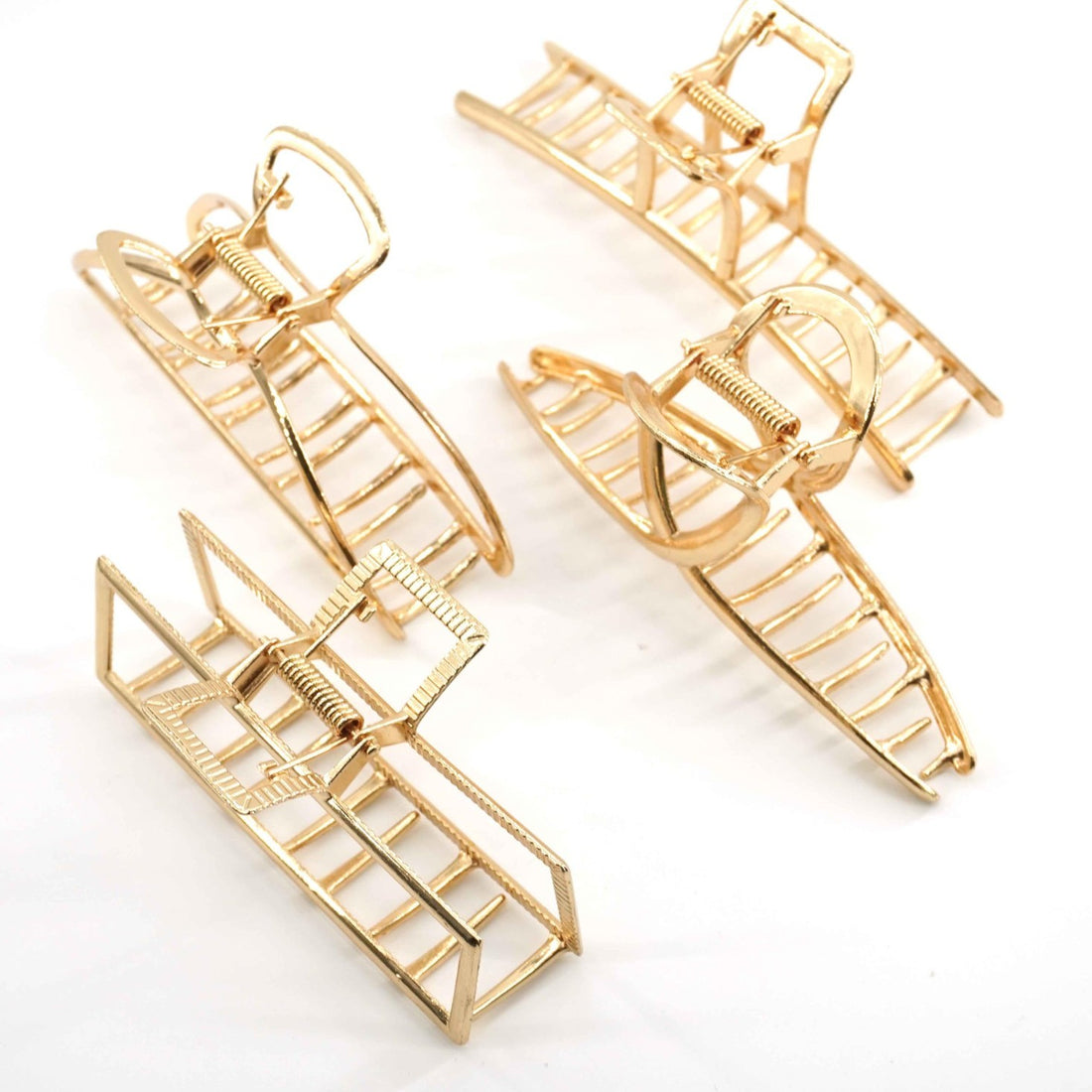 Four gold metal large hair claw clips arranged on a flat surface, showing interlocking teeth and alloy construction