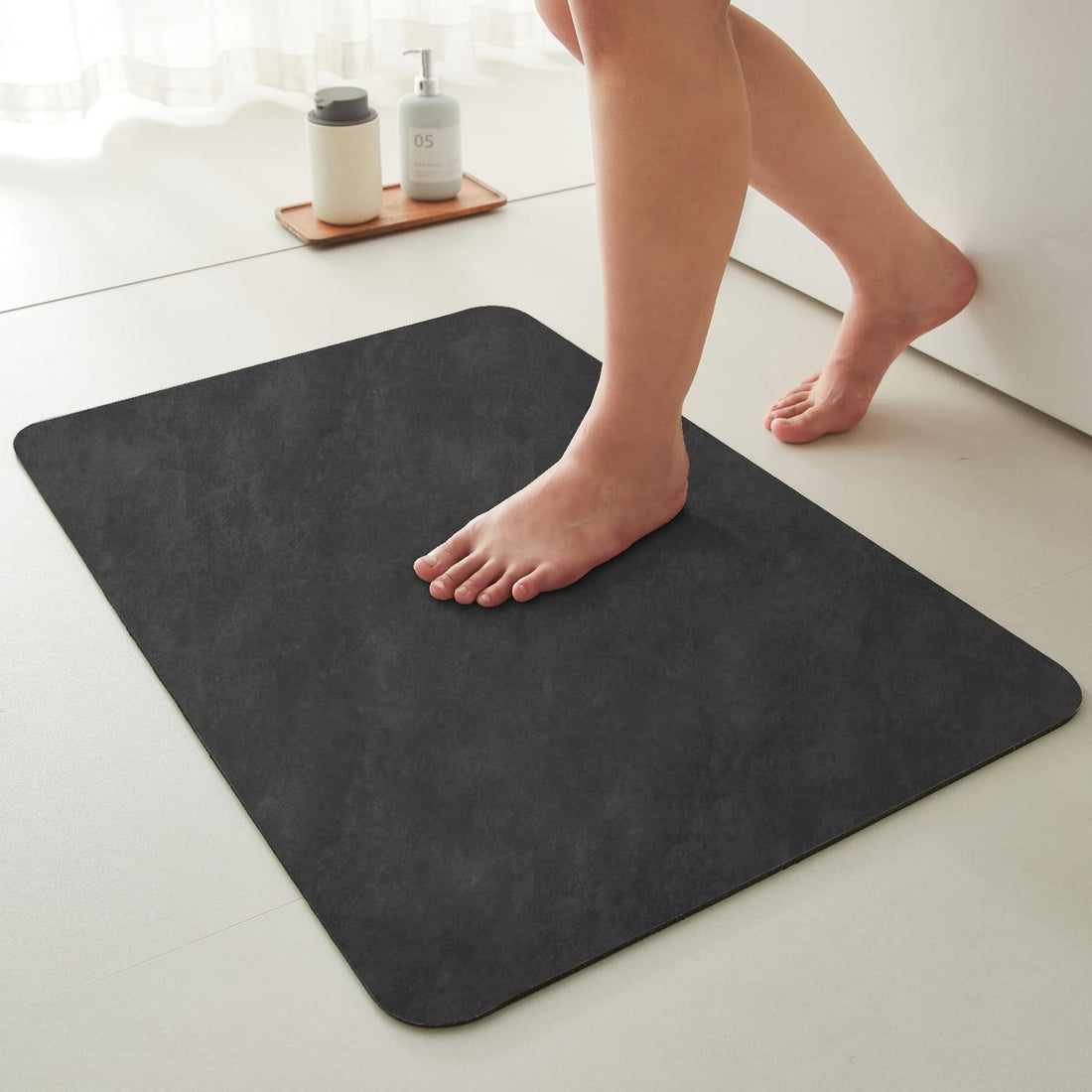 Black 16x24 inch rectangular bath mat with faux suede surface and natural rubber non-slip backing on bathroom floor